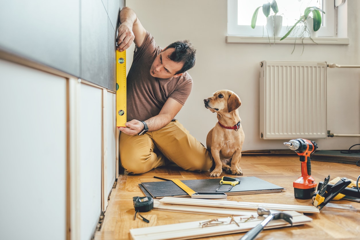 Man doing a DIY home renovation project while his dog watches.