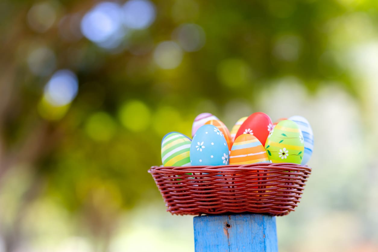 A basket filled with colorful painted Easter eggs, set against a backdrop of natural trees, evoking the joy of Easter.