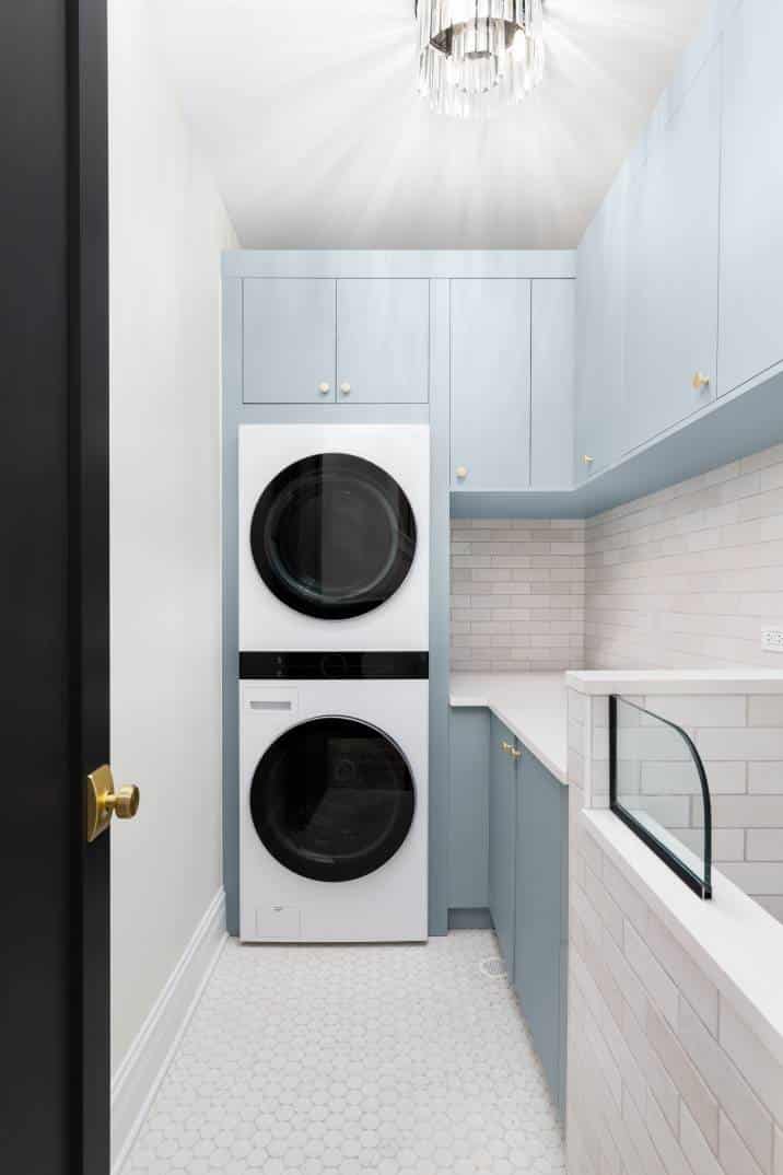 A laundry room with blue cabinets, white washer and dryer, circular tile flooring, subway tile backsplash, and a chandelier hanging above