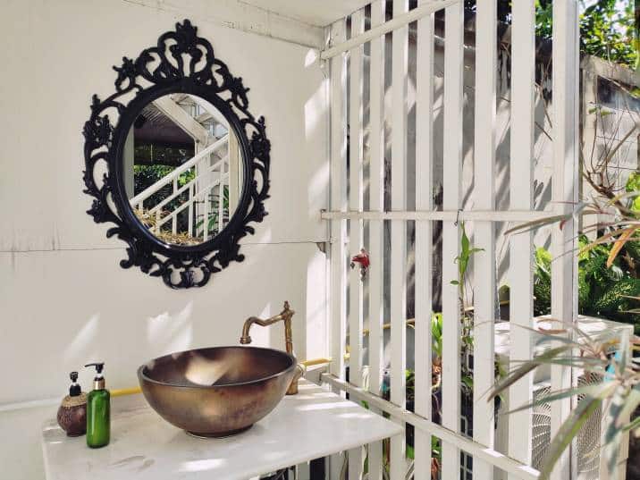 beautiful outdoor round brass basin laundry sink in vintage style with vintage black mirror, in sunlight through the white wooden partition in the garden