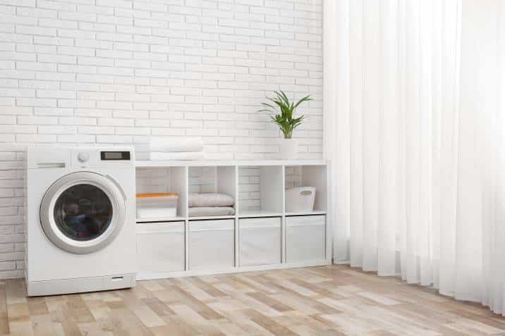 modern washing machine beside hamper cubbies, brick wall in laundry room