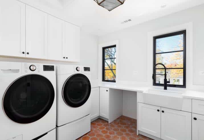 laundry room with red hexagon-patterned tiles, white cabinets and appliances 