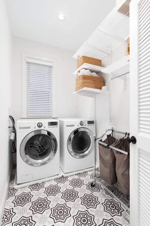 A laundry room with a patterned tile floor, white washer and dryer, and organised shelving on the wall