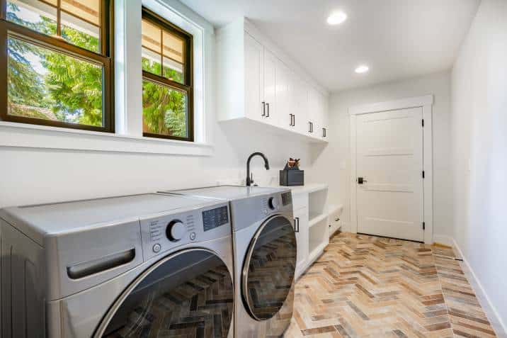 large laundry room with stainless washer and dryer on chevron tiles, parquet wood floors