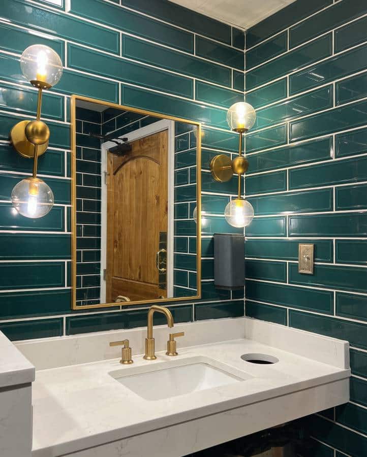 laundry room sink with green subway-style tiles on wall, gold lights, marble sink and a gold faucet