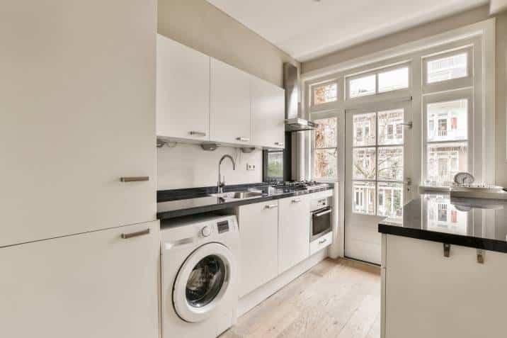 Small white kitchen laundry room with stylish tiles, black countertop and sink with faucet. Scandinavian interior