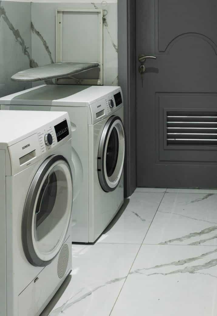 grey and white laundry room with marble floor, two washing machines against the wall 