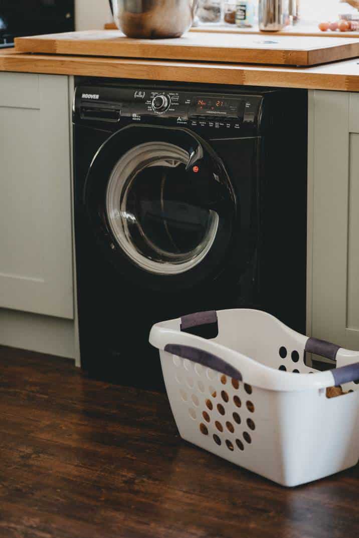 a black washing machine under a wooden kitchen countertop, laundry basket sitting next to the washing machine
