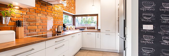 Bright and clean modern minimalist kitchen with white cabinets, brick wall and glass splashback