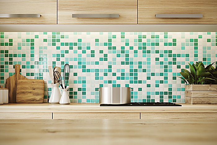 Close up of a light hardwood table surface in a kitchen with green and white mosaic walls, wooden consoles and a cooker