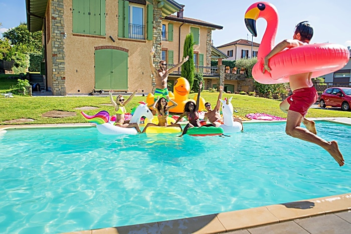 Multiracial group of friends having party in a private villa with swimming pool - Happy young people chilling with shaped air mattresses