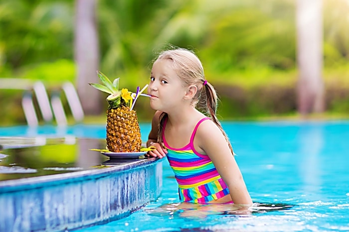 Child drinking juice in swimming pool bar. Summer family 