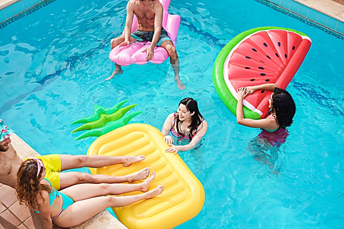 Happy friends having fun inside swimming pool during summer vacation on citrus floats