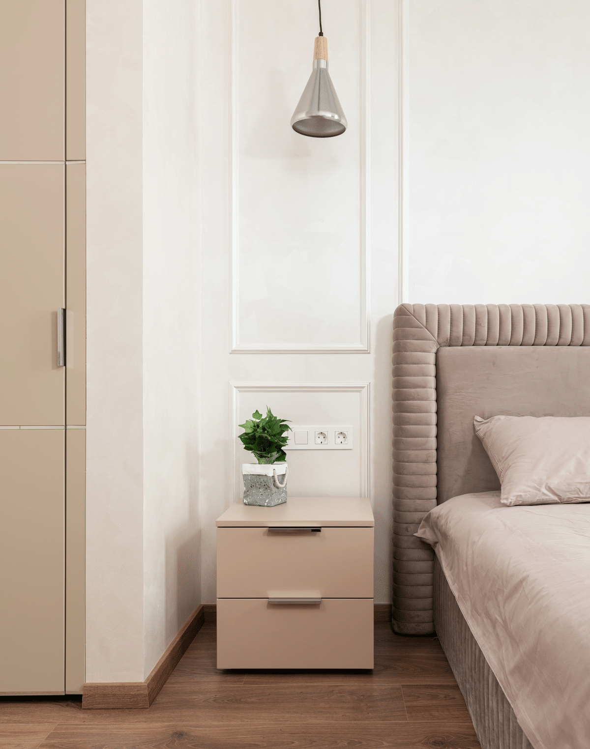 bedside table with a plant on it and a cone-shaped lamp suspended above