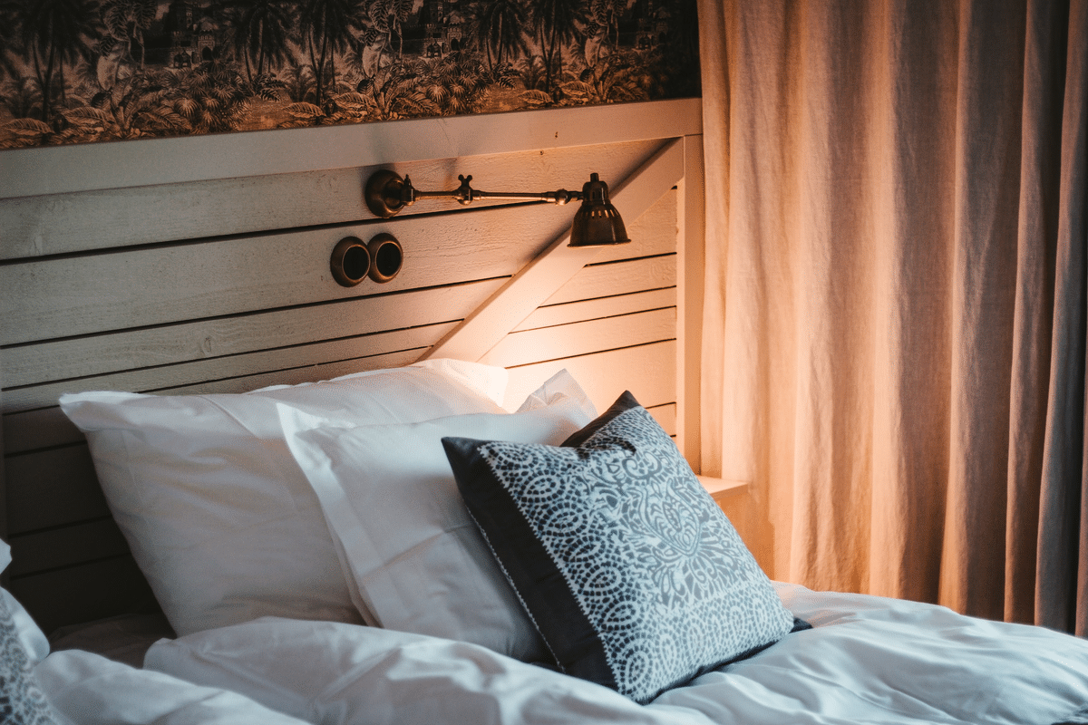three pillows on a bed with a small vintage lamp attached to wooden headboard
