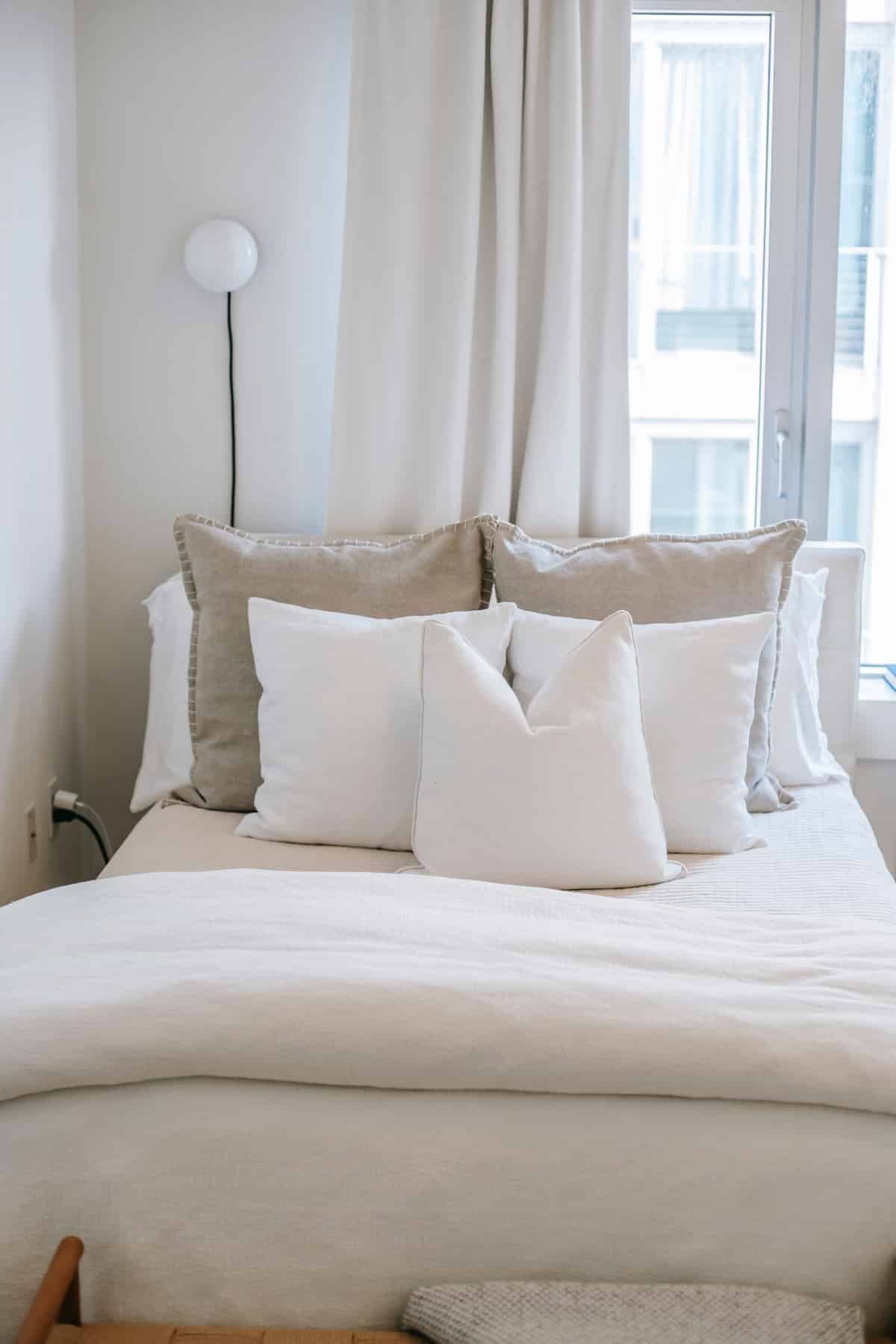 Cosy bedroom with white pillows and bedding beside window