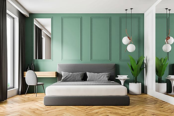 Interior of modern bedroom with green walls, wooden floor, gray master bed and make up table in the corner. 