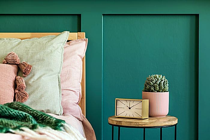 Stylish bedroom interior with design coffee table, plant, gold clock and elegant personal accessories. Beautiful bed sheets, blanket and pillows.