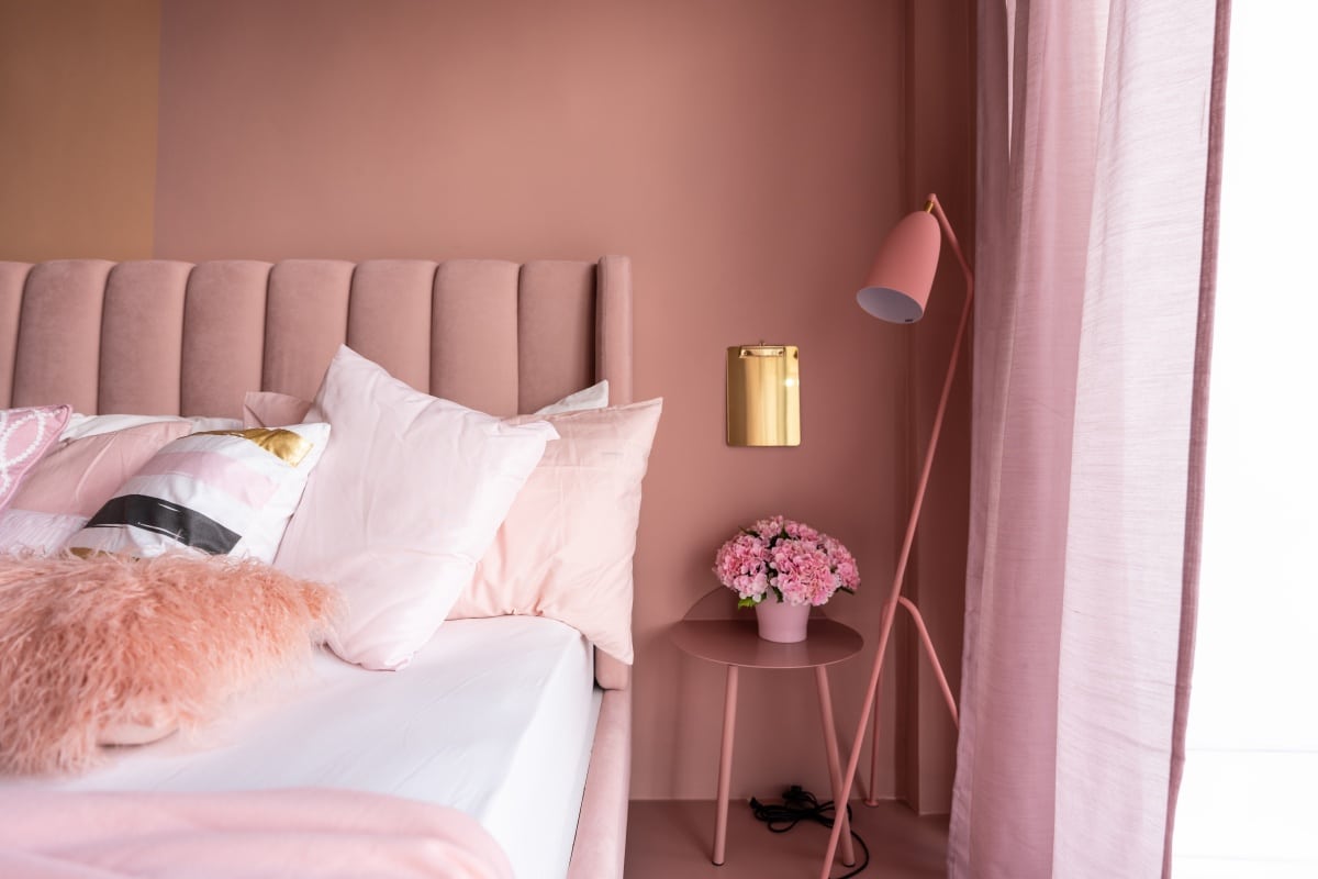 Cozy pink bedroom corner with baby pink velvet fabric bed decorated by blanket, pillows and pink floor lamp