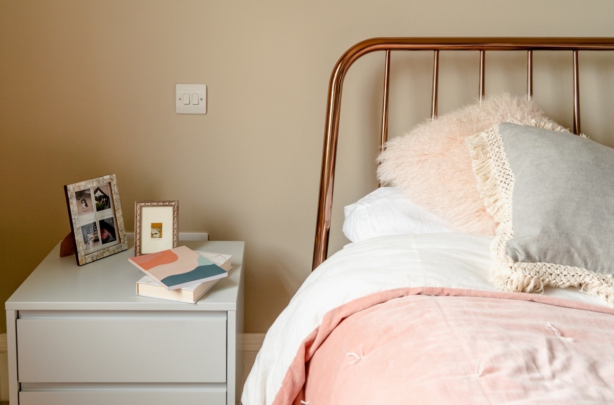 Grey nightstand next to a bed with pink sheets