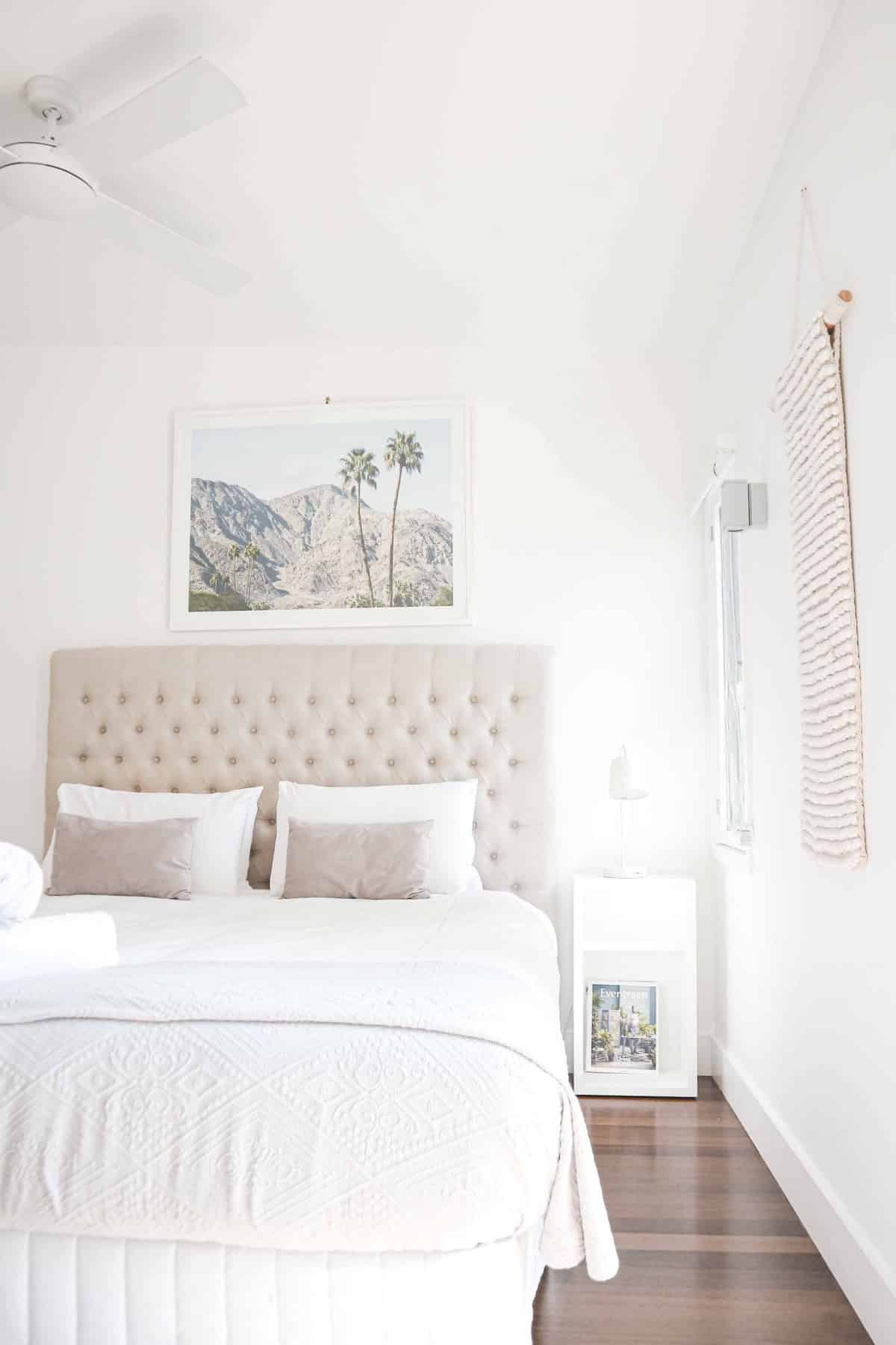 white bedspread with an off-white upholstered headboard in a room with wood floors