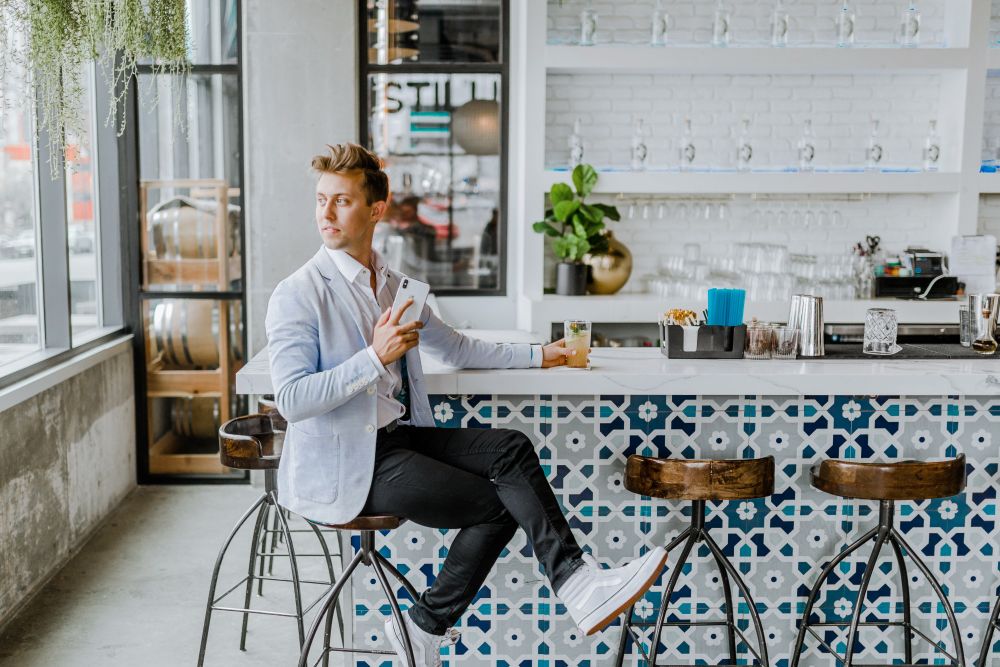 blond man sitting on bar stool at home with drink in hand