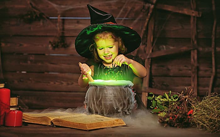 Halloween. little witch child cooking potion in the cauldron with spell book