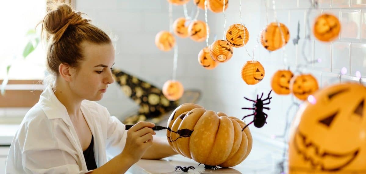 Autumn leaves. Autumn party decorations. sitting behind a table in Halloween theme decorated kitchen, holding hand painted pumpkins