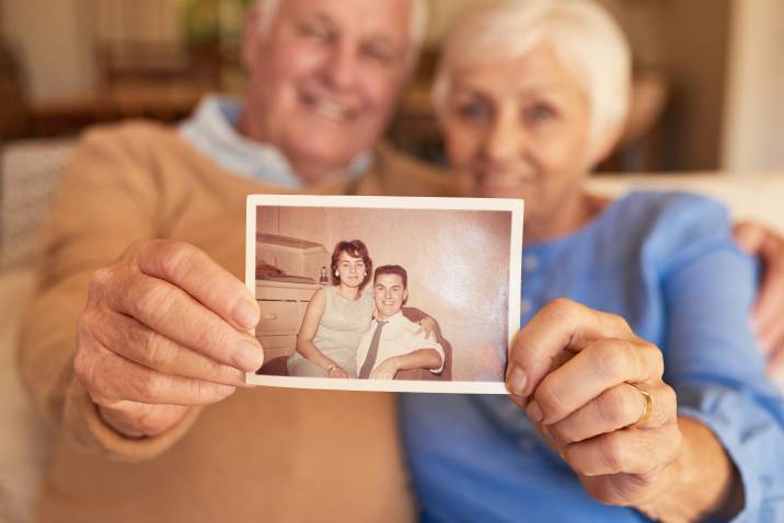 senior couple holding up a restored old photograph of themselves when they were young