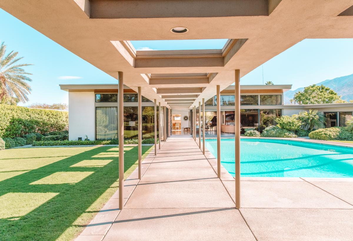 Symmetrical photo of concrete walkway canopy with skylight panels. Swimming pool and grass on either side of walkway