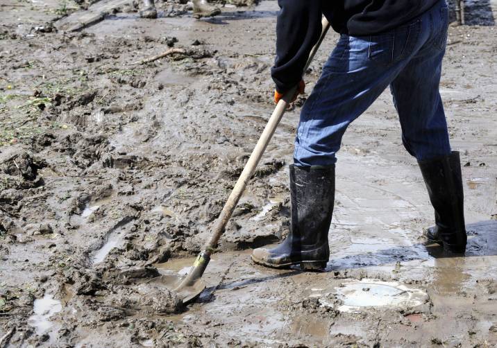 man cleaning up mud with a shovel after a flood