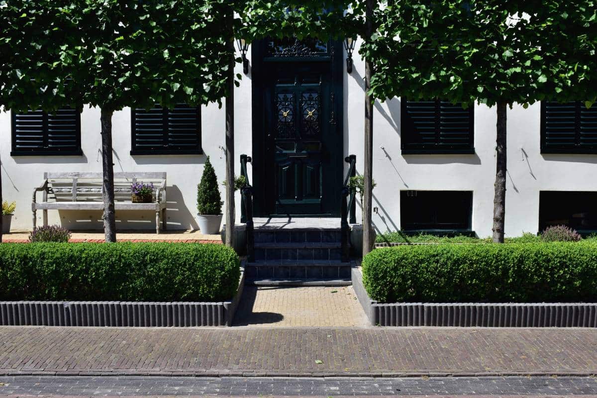 facade of a house with closed shutters, symmetrical hedges by the entrance