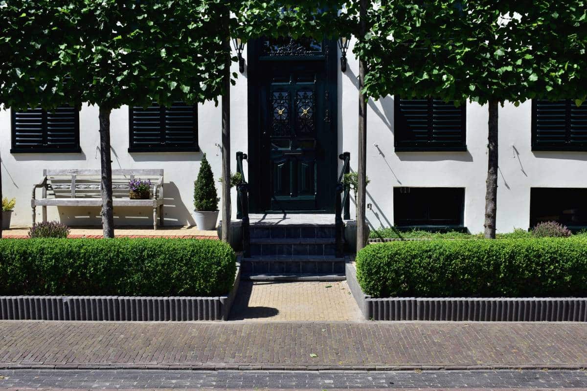 facade of a house with closed shutters, symmetrical hedges by the entrance 