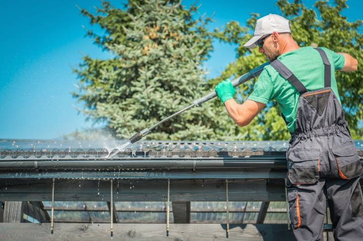 a handyman power cleaning a roof gutter with a pressure washer