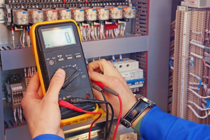 Closeup of electrical tester in the hands of an electrician testing a control cabinet 