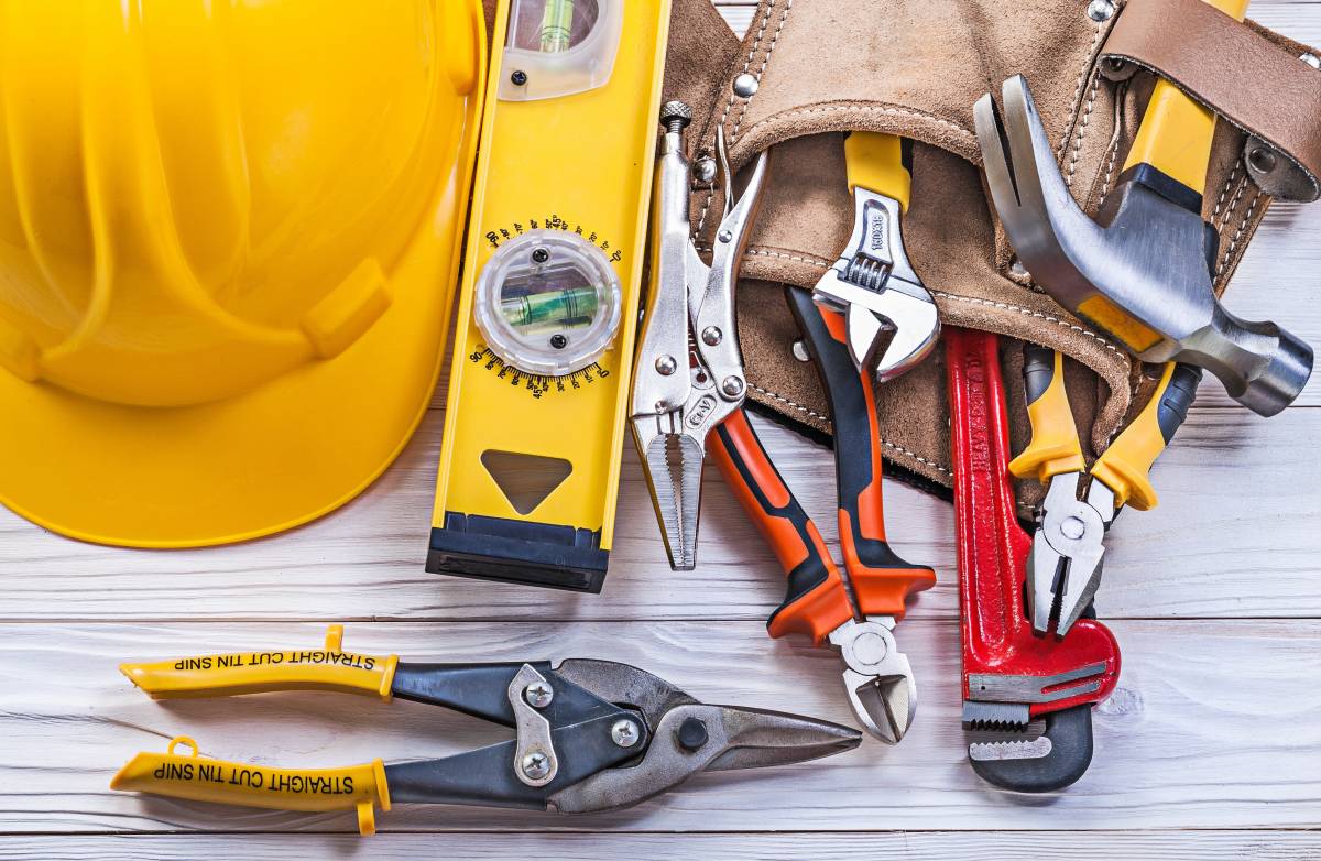 Composition of essential handyman tools in leather tool belt, with building helmet on wooden board