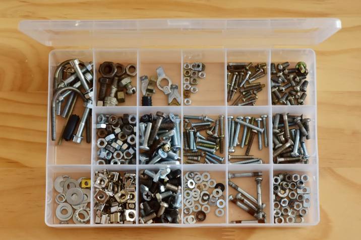 Plastic transparent organizer with various bolts nuts on a wooden surface