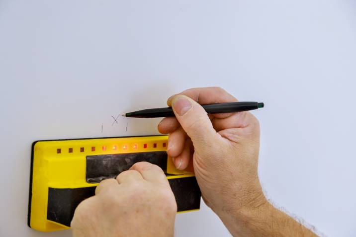 Man using a digital stud finder, detector to scan a wooden wall 
