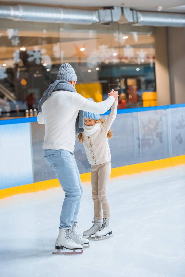 a dad teaching his daughter ice skating in an indoor ice rink