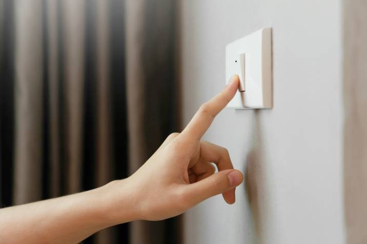 Closeup finger turning off light switch to save money on electricity bill