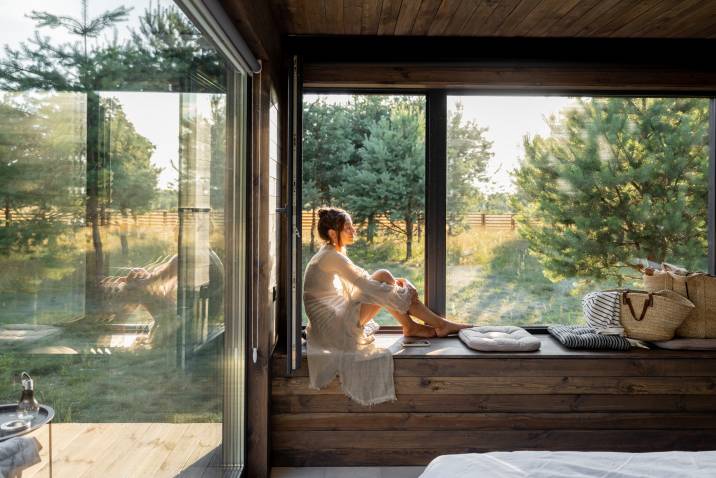 Young female house sitter sitting on a window sill at beautiful country house, house sitting to earn money during spring 