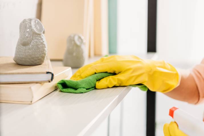 Spring cleaning, cropped view of woman in yellow rubber gloves cleaning book shelf 