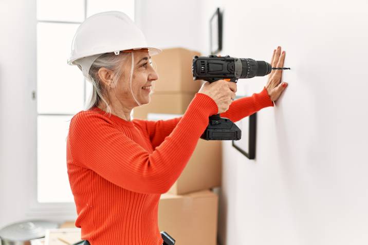 confident grey-haired woman drilling wall, home improvement as a side hustle for retirees