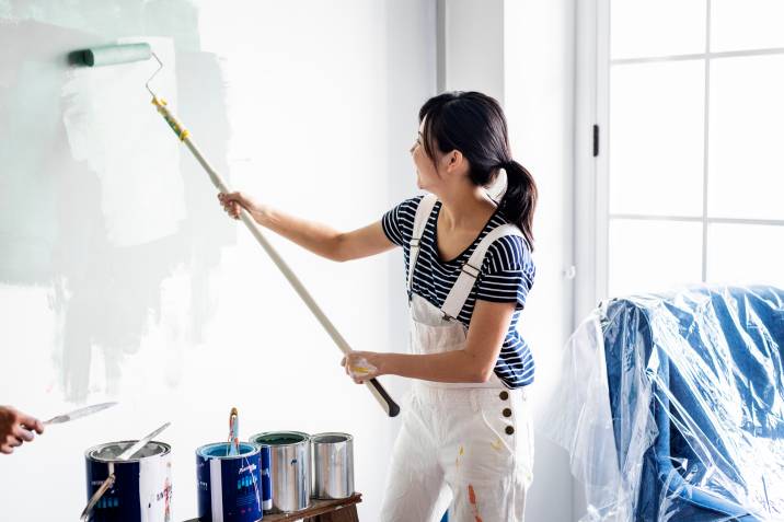 woman painting house wall with a roller during winter to earn extra cash