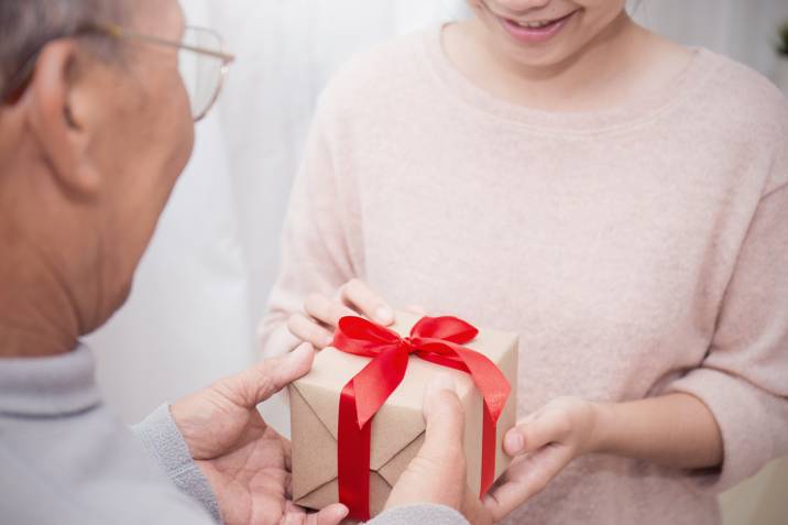 senior old man delivering a gift to a smiling young woman