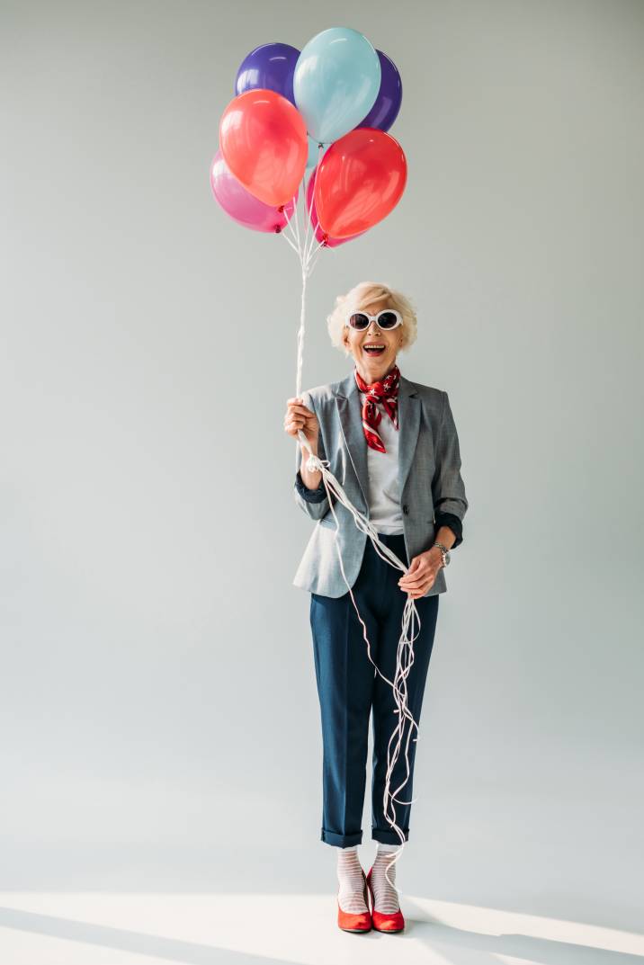 stylish senior woman modelling in sunglasses while holding balloons