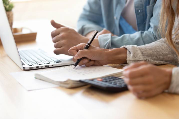 Spouses calculating income and expenses of client using calculator, notebook, and laptop. Office admin job from home