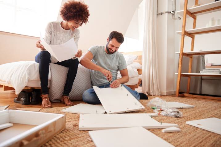 Furniture assembly side hustle. Couple assembling a cabinet. Woman holding the instructions while the man puts screws into a cabinet panel