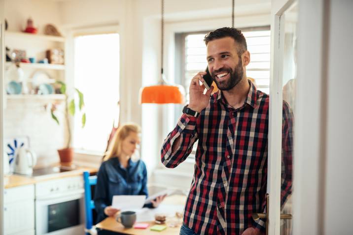 Smiling man talking to client on the phone while his wife reads paper documents and prepares reports. Virtual assistant job