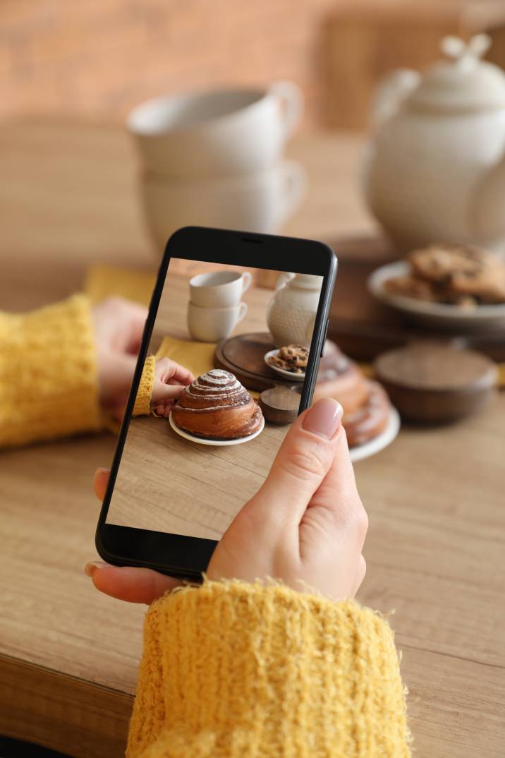 Taking stock photos to sell online. Female food photographer with mobile phone taking picture of cinnabon on table